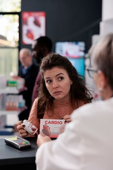 Portrait of woman customer standing at drugstore counter discussing health care treatment with pharmacist, wanting to buy cardiology pills. Drugstore worker offering medicine service and support