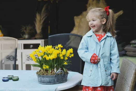 A girl in a dress near a pot of daffodils
