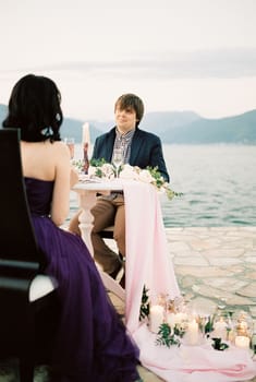 Woman and man are sitting at a laid festive table on the pier. High quality photo