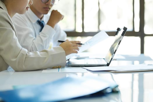 Close up businesspeople or colleagues are working together on investment project, discussing, sharing ideas, planning, and analyzing the business strategy and finance using laptop and graphs at workplace.