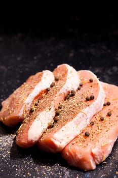 Close up view on uncooked meat seasoned with spices, pepper and salt on dark wooden board