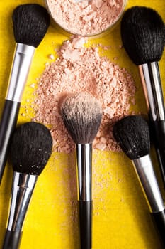 Different type of make up brushes and spread powder on yellow paper background