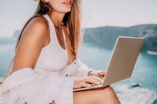 Digital nomad, Business woman working on laptop by the sea. Pretty lady typing on computer by the sea at sunset, makes a business transaction online from a distance. Freelance remote work on vacation