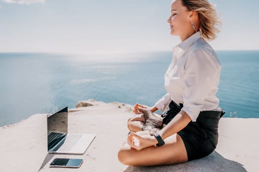 Happy girl doing yoga with laptop working at the beach. beautiful and calm business woman sitting with a laptop in a summer cafe in the lotus position meditating and relaxing. freelance girl remote work beach paradise