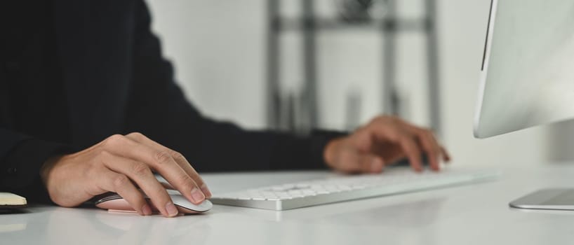 Cropped image of man typing on wireless keyboard, office worker working on white office desk.