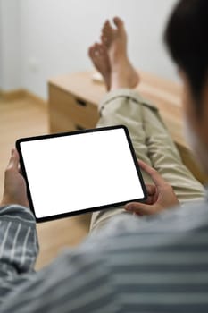 Over shoulder man in casual cloth putting legs on table and using digital tablet.