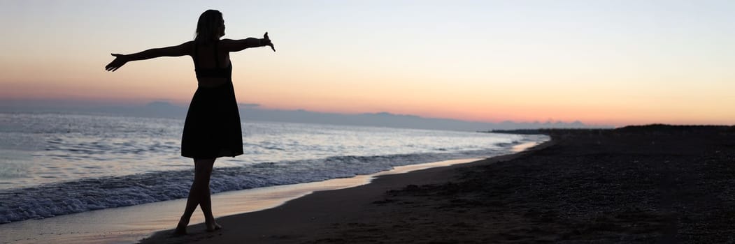 Woman standing with open arms on seashore at sunset. Beautiful life concept