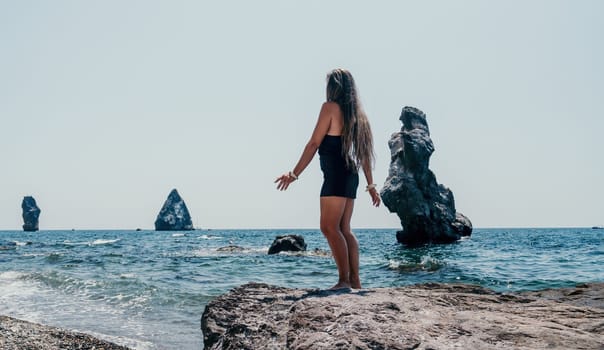 Woman travel sea. Young Happy woman in a long red dress posing on a beach near the sea on background of volcanic rocks, like in Iceland, sharing travel adventure journey