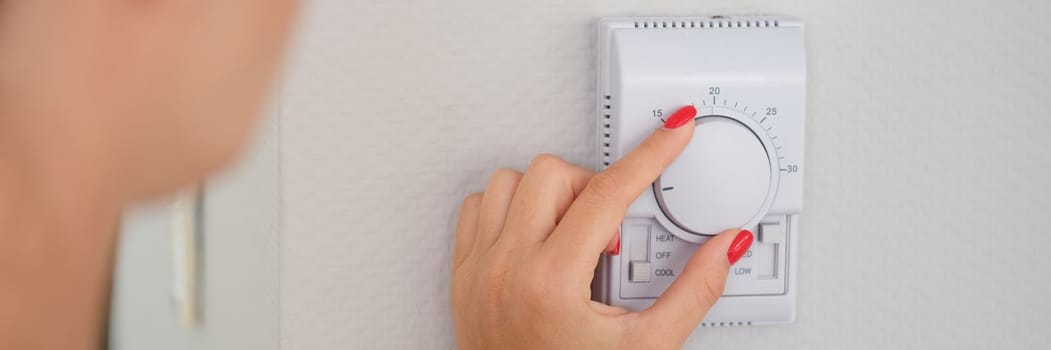 Hand adjusts button of the control unit of heating and cooling system of house closeup. Home or office climate control