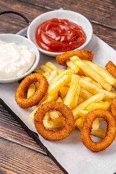 Onion rings and french fries with ketchup and mayonnaise on wooden table