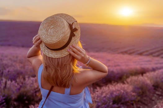 Woman lavender field sunset. Romantic woman walks through the lavender fields. illuminated by sunset sunlight. She is wearing a blue dress with a hat