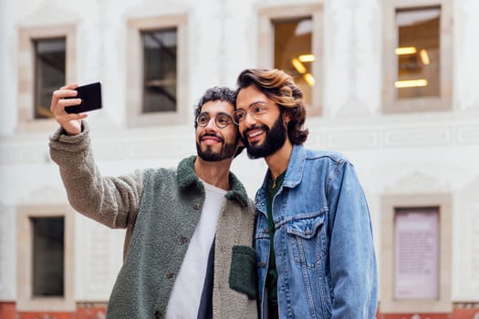 gay male couple taking a selfie photo with their mobile phone in the street, concept of urban lifestyle and love between people of the same sex, copy space for text