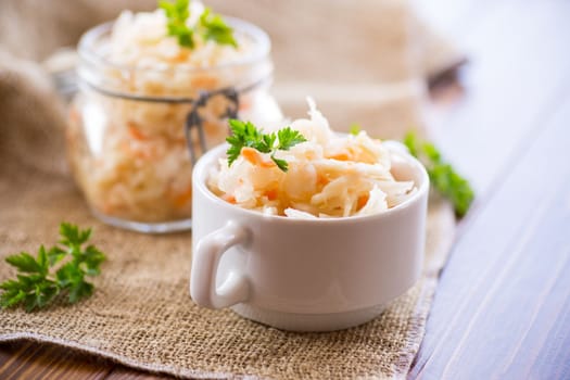 Sauerkraut with carrots and spices in a bowl on a wooden table.