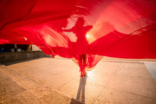 Sunrise red dress. A woman in a long red dress against the backdrop of sunrise, bright golden light of the sun's rays. The concept of femininity, harmony