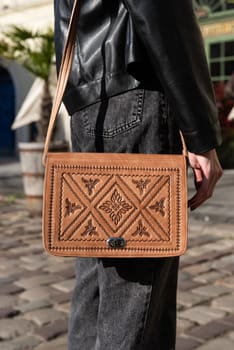 small brown women's leather bag with a carved pattern. street photo