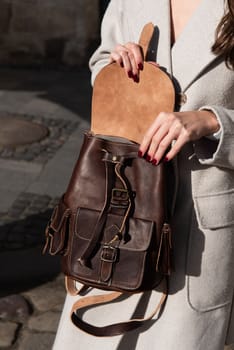 young girl wearing beige coat posing outside with a leather backpack