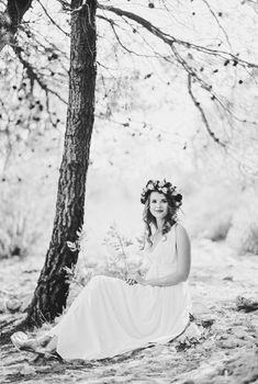 Bride in a wreath on her head sits under a tree. Black and white photo. High quality photo