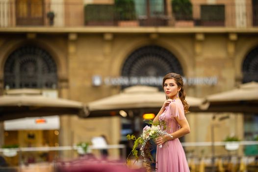 A bride in a pink dress with a bouquet stands in the center of the Old City of Florence in Italy.