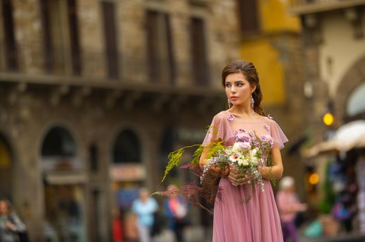 A bride in a pink dress with a bouquet stands in the center of the Old City of Florence in Italy.