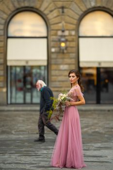 A bride in a pink dress with a bouquet stands in the center of the Old City of Florence in Italy.