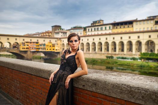 Beautiful stylish bride in a black dress stands on the embankment in Florence, Italy.