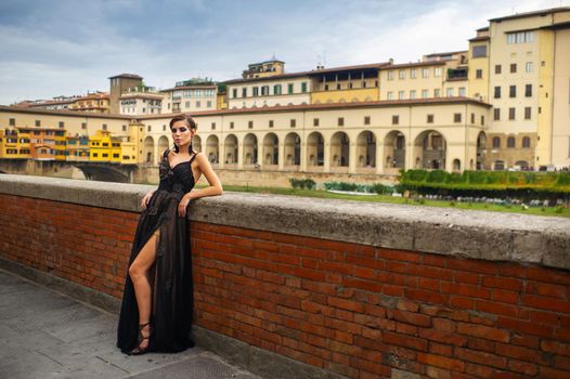 Beautiful stylish bride in a black dress stands on the embankment in Florence, Italy.