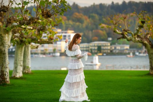 A bride in a white wedding dress in a park in an Austrian town with large trees at sunset.