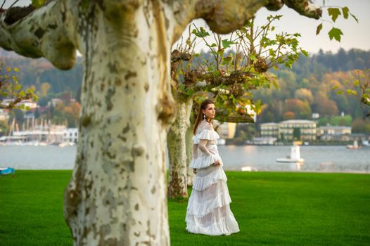 A bride in a white wedding dress in a park in an Austrian town with large trees at sunset.