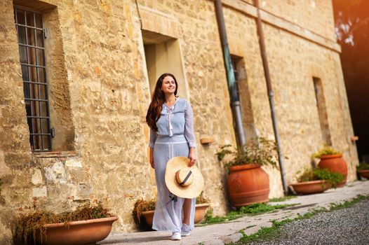 A girl in a dress and hat walks in the afternoon in an Italian town in Tuscany.