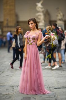 A bride in a pink dress with a bouquet stands in the center of the Old City of Florence in Italy.