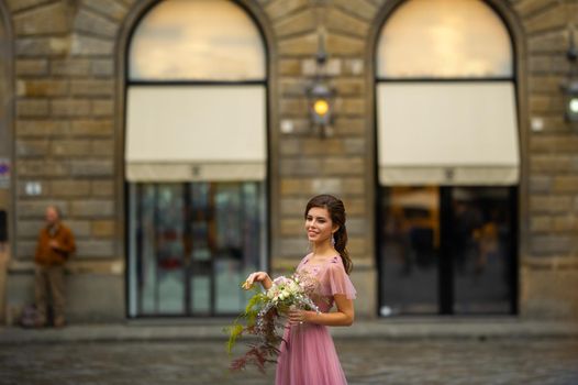 A bride in a pink dress with a bouquet stands in the center of the Old City of Florence in Italy.