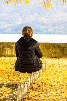 Autumn leaves fallen on standing alone woman on the autumn alley. Autumn landscape, orange foliage in a park in Orsova, Romania, 2020