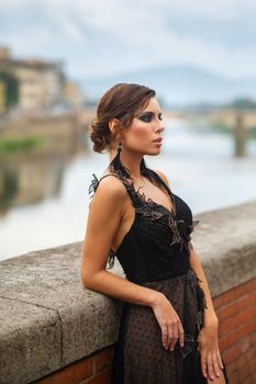 Beautiful stylish bride in a black dress stands on the embankment in Florence, Italy.