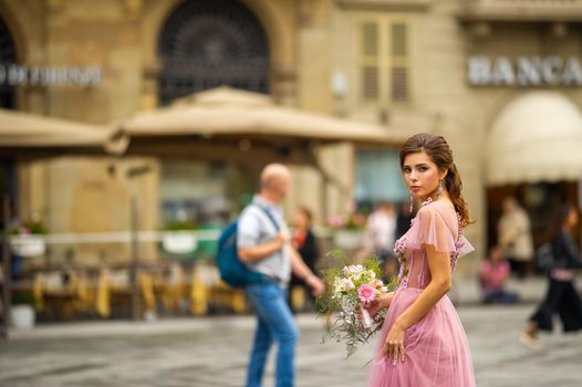 A bride in a pink dress with a bouquet stands in the center of the Old City of Florence in Italy.