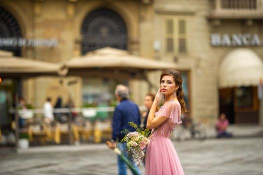 A bride in a pink dress with a bouquet stands in the center of the Old City of Florence in Italy.