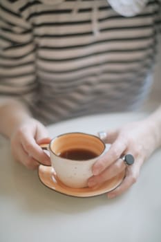 Woman's hands holding cup of hot drink coffee indoors. Still life composition.