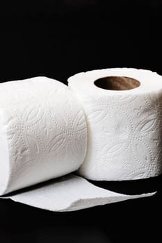 Two rolls of white toilet paper on a black background close up