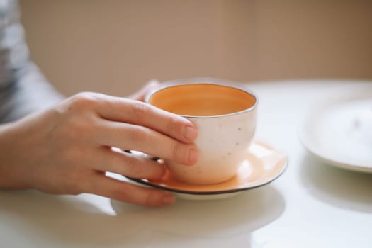 Woman's hands holding cup of hot drink coffee indoors. Still life composition.