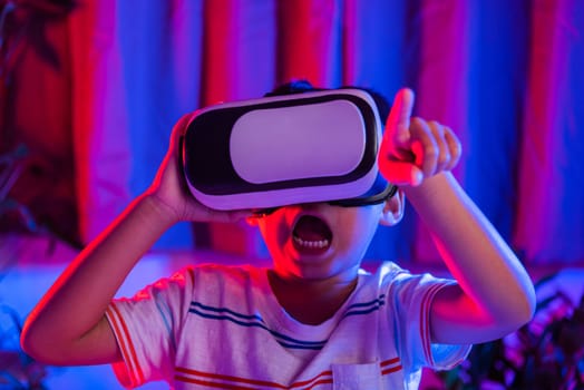 Asian little kid boy wearing virtual reality goggles experiencing reality, Child wear VR helmet excited open mouth at home dark purple and blue background, Virtual technology