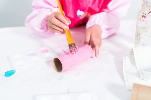 Little girl making a unicorn out of the toilet paper roll and craft paper.