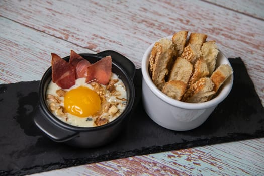 Recipe Oeuf cocotte with fresh cream sauce, Roquefort and walnuts, ham chips, toasted bread sticks. High quality photo
