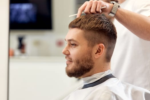 handsome young man visiting professional hairstylist in barber shop