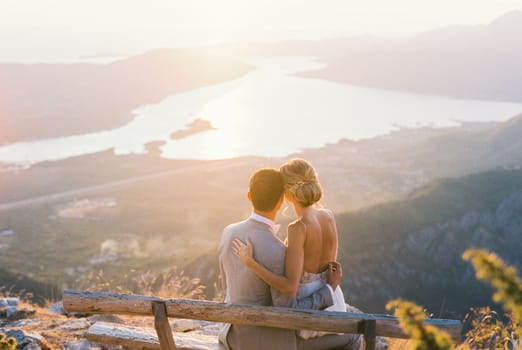 Bride sits on groom lap on a bench on the mountain. Back view. High quality photo
