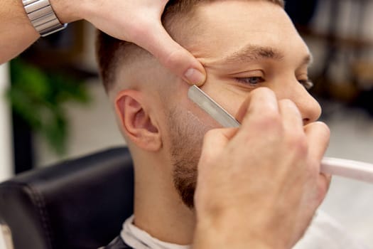 Barber shaving bearded man with retro knife in barber shop. close-up