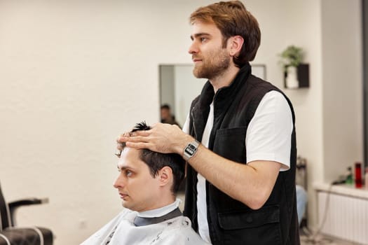 Professional hairdresser does haircut for caucasian client man at barber shop.