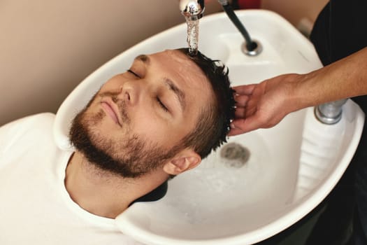 Barber washing hair of caucasian man in barber shop