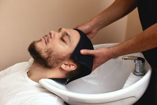 Barber washing hair of caucasian man in barber shop
