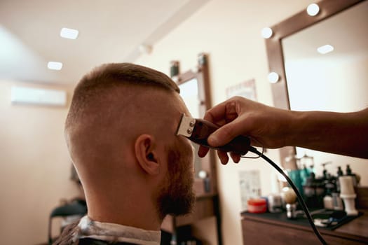 Barber shaving handsome bearded man in barber shop.