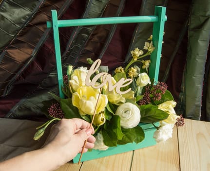 Female hand holding a wooden topper with the word Love around the box with the beautiful spring flowers.