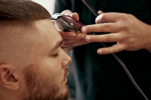 Barber shaving handsome bearded man in barber shop.